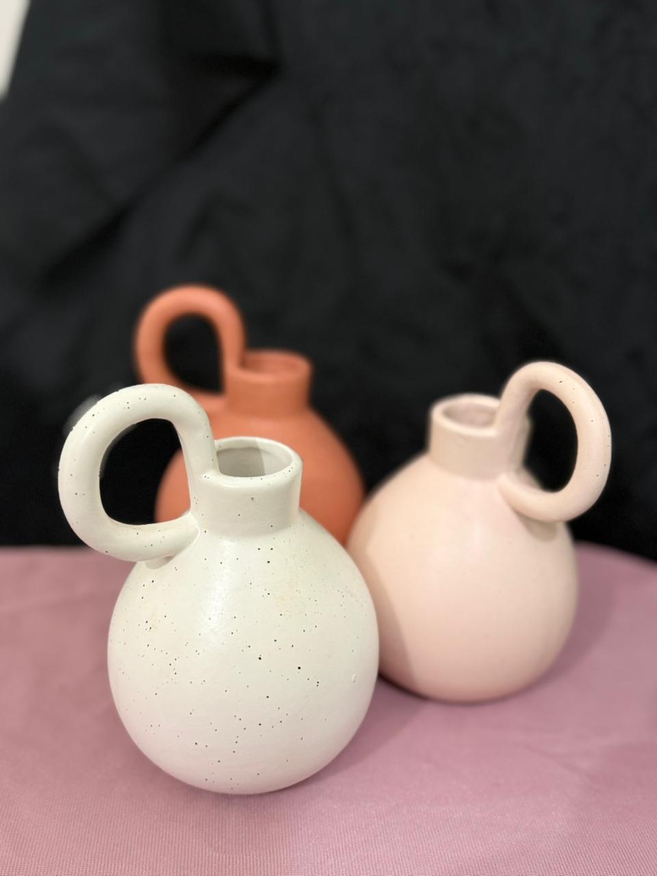 Three ceramic vases with handles on a pink surface against a black background